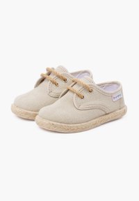 Chaussures en toile beige à bout rond, lacets marron clair et semelle en corde de jute. Éléments de couture minimaux et petit logo de marque coloré.