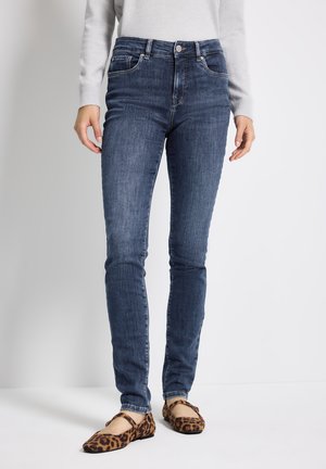 Jean skinny en denim bleu foncé avec une taille mi-haute, des poches avant et une décoloration subtile. Associé à des chaussures plates à imprimé animal.