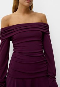 Off-the-shoulder purple dress with long sleeves, featuring textured ruching throughout, smooth fabric, and a form-fitting silhouette.
