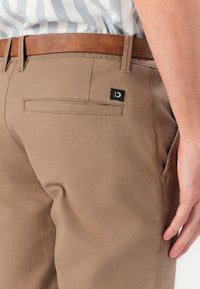 Khaki kalhoty vyrobené z lehké tkaniny, s plochou zadní kapsou, jemným šitím a hnědým koženým pásem.