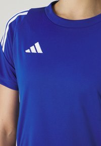 Blauw sport T-shirt van soepel materiaal, met witte horizontale strepen op de schouders en een wit logo op de borst.