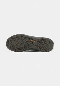 Suela de un zapato negro para exterior con tacos profundos y angulares y un pequeño logo naranja de Continental en el centro.