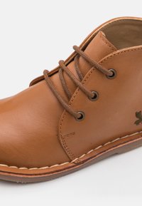 Zapato de cuero marrón con punta redonda, costuras visibles, cordones marrones y ojales de metal; presenta un detalle bordado en verde en el lateral.