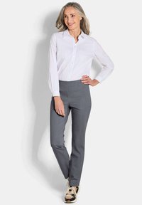 Witte blouse met lange mouwen, grijze op maat gemaakte broek en patroon sneakers. De outfit heeft een getailleerde snit en gladde texturen.