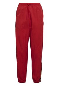 Červené lehké tepláky s elastickým pasem, vybavené bočními kapsami a kontrastními pruhovanými detaily po stranách.