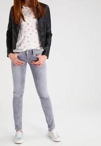 Černá kožená bunda, bílá košile s hvězdným vzorem, šedé slim-fit džíny a šedé tenisky s bílými akcenty. Jednoduchý, moderní městský outfit.