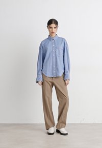 Camicia in denim azzurro chiaro con bottoni e taschino sul petto, abbinata a pantaloni beige a gamba larga e scarpe bianche con tacco piattaforma. Tessuto liscio in tutto il capo.
