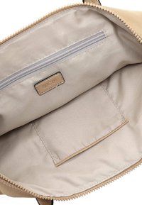 L'interno della borsa beige chiaro presenta una tasca con zip e una tasca a filetto, realizzato in un tessuto liscio con dettagli cuciti e un'etichetta con il logo.