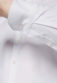 Weißes Baumwoll-Hemdkleid mit glatter Textur. Verfügt über einen geknöpften Ärmel und zwei sichtbare Knöpfe am Ärmel und an der Blende.