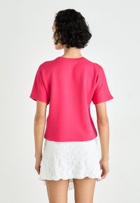 Haut rose à manches courtes en tissu lisse, avec un col arrondi et une coupe décontractée, associé à une jupe en dentelle blanche.