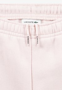 Ανοιχτό ροζ παντελόνι φόρμας Lacoste μ�ε ελαστική μέση, ετικέτα λογότυπου και κορδόνια. Μαλακή υφή και ριμπ λεπτομέρειες.