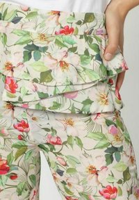 Pantalones florales con un fondo crema, que presentan detalles de volantes en capas y patrones florales vibrantes en rosa y verde. Tela ligera y transpirable.