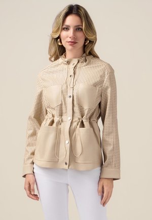 Beige perforierte Jacke mit tailliertem Schnitt, zwei Vordertaschen und Kapuze mit Kordelzug; glatte Textur, Druckknöpfe und lange Ärmel.