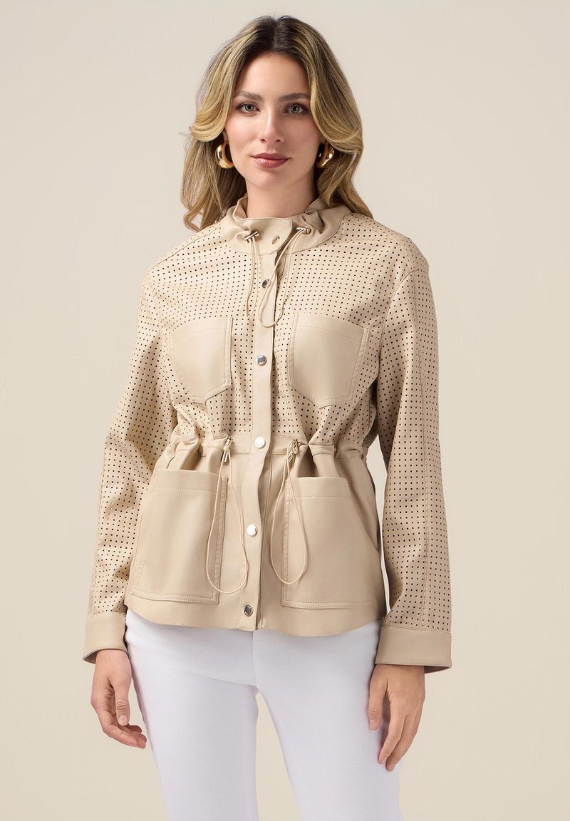 Beżowa perforowana kurtka z wąskim paskiem w talii, podwójnymi przednimi kieszeniami i kapturem ze sznurkiem; gładka tekstura, napy i długie rękawy.