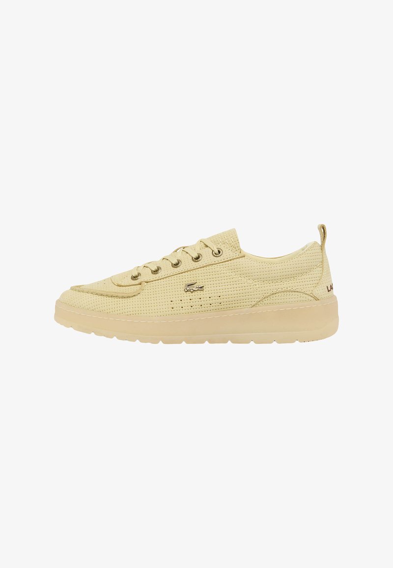 Zapatilla deportiva perforada de color amarillo claro con diseño de cordones, suela de goma tonal y sutil detalle de logo. Textura suave y forma de punta redondeada.