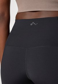High-waisted black leggings made from stretch fabric, featuring a smooth texture and subtle logo at the waistband.