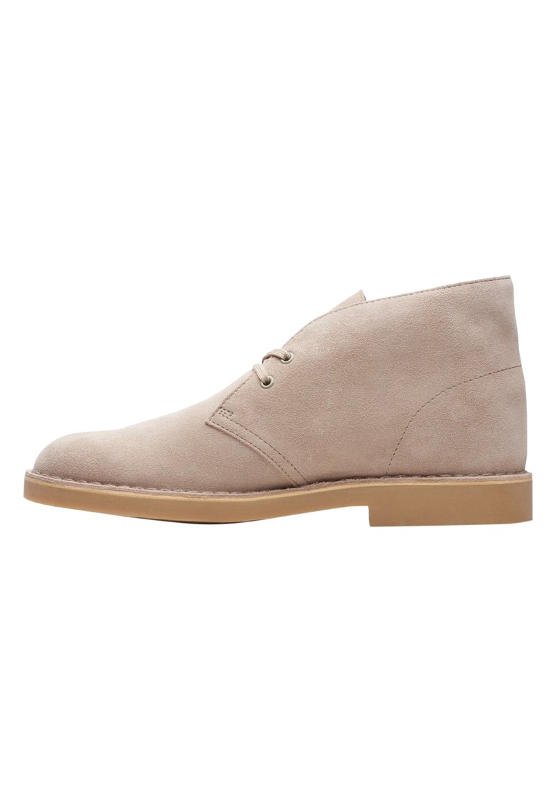 Beige mockaskänga med rund tå, två snörningsöppningar och en låg tan gummisula. Har en slät yta och minimal sömdekoration.