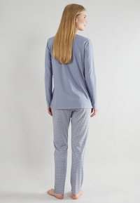 Top a maniche lunghe blu chiaro abbinato a pantaloni del pigiama grigi e bianchi a quadri. Tessuto morbido, vestibilità rilassata e consistenza soft in tutto il capo.