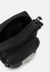 Borsa a spalla in tessuto nero con più scomparti con zip, superficie testurizzata e un'etichetta con logo a contrasto sul davanti.