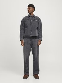 Mørk grå denimjakke med to brystlommer og knapper, kombinert med matchende løstsittende bukser og brune sko. Glatt tekstur, uformell design.