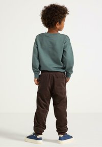 Turkis sweatshirt og brune corduroy bukser. Sættet har en løs pasform, ribbede manchetter og baglomme detalje på bukserne.