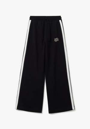 Pantalones de chándal amplios y negros con rayas laterales blancas y una cintura elástica. Presenta un cordón y el logo "USA" en bordado blanco.