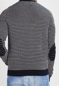 Pull en maille avec un motif de points alternés noirs et blancs, doté d'un col et de poignets côtelés, avec une bande inférieure unie noire.