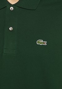 Polo vert en coton texturé, doté d'une patte de boutonnage à trois boutons et d'un petit logo de crocodile brodé sur la poitrine.