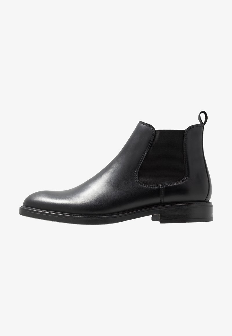 Botte Chelsea en cuir noir avec panneau latéral élastique, talon bas, bout rond et languette à l'arrière, vue de profil sur fond blanc.