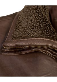 Bruine leren jas met een kraag van bruin fleece, voorzien van een rits langs de rand. Gladde textuur met zichtbare stikdetails.