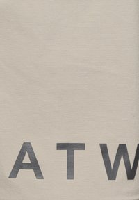 Częściowy widok czarnych wielkich liter "A T W" nadrukowanych na jasnobeżowym tle z tkaniny.