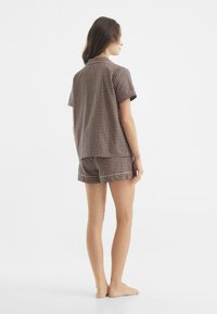 Pijamas a cuadros marrones y beiges con camisa de manga corta y pantalones cortos. Presenta un ajuste relajado y una textura suave, adecuada para el uso informal.