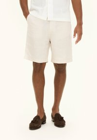 Light beige linen shorts with a relaxed fit, two side pockets, and a hem finishing just above the knee, worn with dark brown loafers.