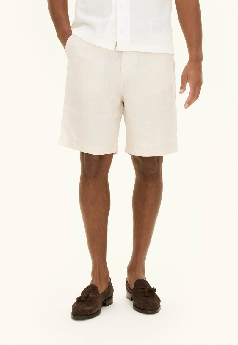 Light beige linen shorts with a relaxed fit, two side pockets, and a hem finishing just above the knee, worn with dark brown loafers.