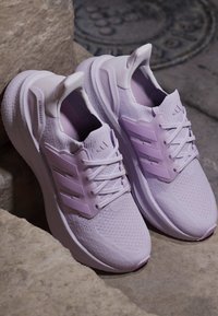 Двойка светлолилави маратонки Adidas Ultraboost, почиващи на каменни стъпала с текстуриран плетен и пластмасови странични ивици.