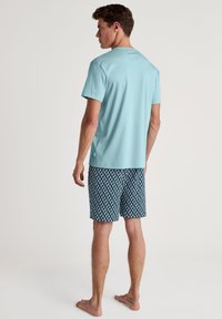 Lichtblauw katoenen t-shirt met ronde hals, gecombineerd met donkere zwemshorts met een patroon in geometrisch ontwerp in het wit.