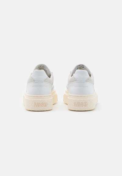 Hvite lær sneakers med grå semsket skinn-detaljer, en tykk teksturert såle, og subtil logo-innprenting på hælen. Rundet design og løfdetass.
