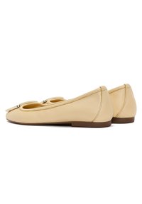 Ballerine in pelle gialla chiara con punta arrotondata e dettaglio a fiocco, suole piatte marroni e cuciture visibili lungo i bordi.