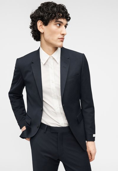 Ανδρικό σακάκι σε ναυτικό μπλε με γιακά με σχισμή, single κουμπί και λευκό πουκάμισο. Διαθέτει λεία υφή και εφαρμοστή ραφή.