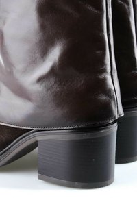 Gros plan de bottes en cuir marron foncé à talons bas sur une surface blanche.