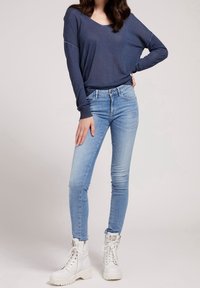 Marineblaues Langarmoberteil mit lockerer Passform, kombiniert mit hellblauen Skinny-Jeans und weißen Kampfstiefeln mit dicken Sohlen und Schnürsenkeln.