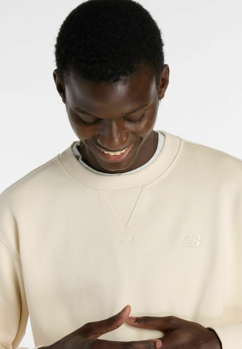 Hellbeiges Sweatshirt mit Rundhalsausschnitt aus weichem Material, mit strukturiertem Ausschnitt und kleinem geprägtem Logo auf der Brust.