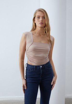 Lys beige topp med firkantet hals og samlet sidesøm, kombinert med mørkeblå høyt liv jeans; glatt stoff og tettsittende design.
