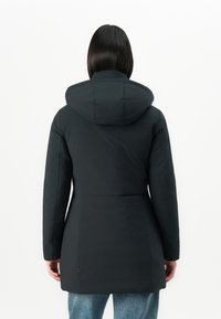Eine Frau trägt einen schwarzen, kapuzenlosen Wintermantel und eine blaue Jeans, von hinten vor einem schlichten weißen Hintergrund gezeigt.