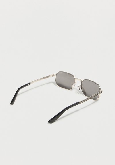 Ορθογώνια γυαλιά ηλίου με ασημί πλαίσιο, σκουρόχρωμους φακούς και μαύρες άκρες στα σκέλη, εμφανιζόμενα από πάνω σε λευκό φόντο.