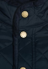 Tessuto trapuntato blu navy con rifiniture in corduroy e tre bottoni a pressione dorati incisi con "Benetton."