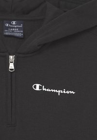 Felpa nera con zip realizzata in morbido tessuto, caratterizzata da un prominente logo "Champion" bianco sul petto, una zip elegante e polsini elasticizzati.
