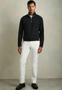 Sudadera negra con cremallera, hecha de un material suave, combinada con pantalones blancos. Presenta un cuello alto y mangas con puños. Botas negras hasta el tobillo completan el conjunto.