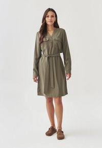 Olive green long-sleeve dress with a collar, button front, two chest pockets, and a matching belt at the waist. Smooth fabric texture.