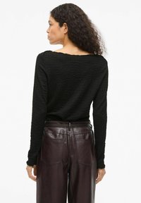 Czarna, teksturowana bluzka z długim rękawem i szerokim dekoltem, zestawiona z głęboko bordowymi skórzanymi spodniami z tylnymi kieszeniami i dopasowanym paskiem w talii.